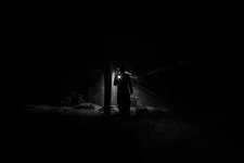 Siluett som lyser med ficklampa i mörkt rum.foto